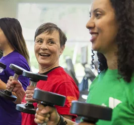 Three women workout together, lifting free-weights, during an exercise class 