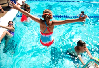 A girl attending summer camp at the West Chester Area YMCA jumps into the outdoor swimming pool during swim time.