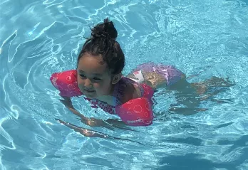 A girls uses a puddle jumper personal flotation device in the outdoor swimming pool