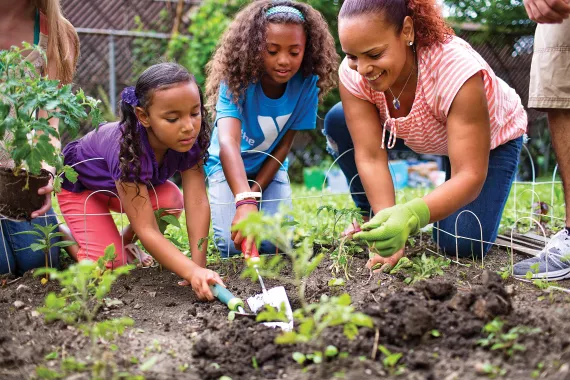 Mother and young kids volunteer and plant in the YMCA vegetable garden.