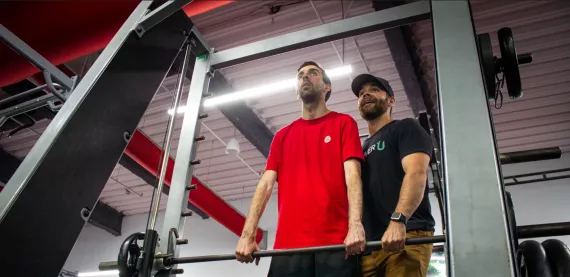 Man lifting weights with training during adaptive fitness session. 