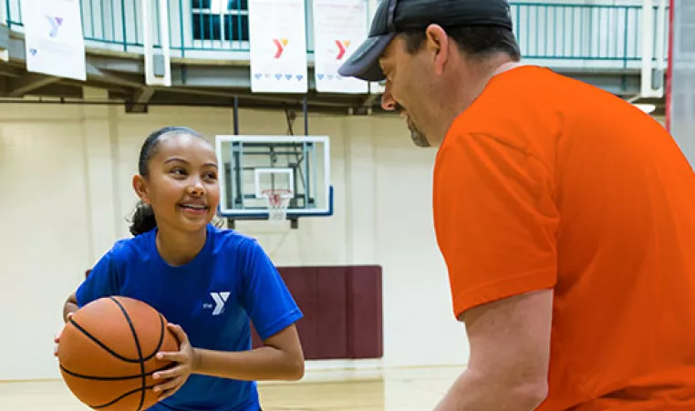 A girl practices basketball drills with her basketball coach at the YMCA