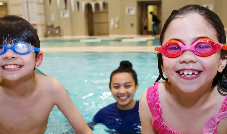 Kids show off their goggles while enjoying a swim lesson with their swim instructor in the indoor swimming pool at the YMCA in Chester County, PA