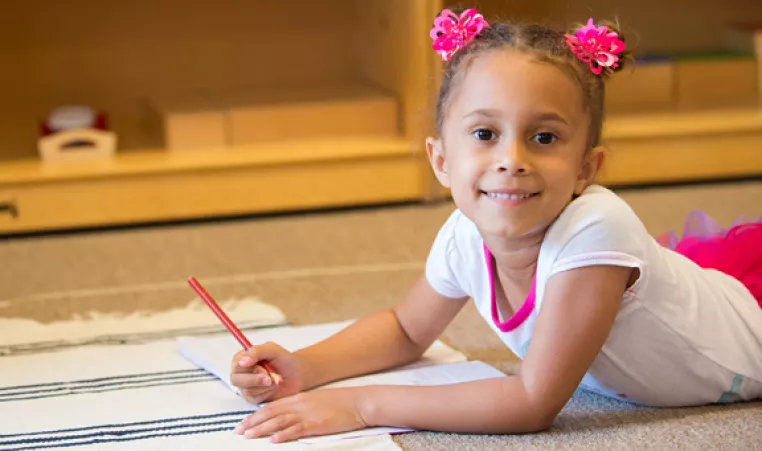 A girl in the West Chester Montessori preschool program smiles while working on an activity.