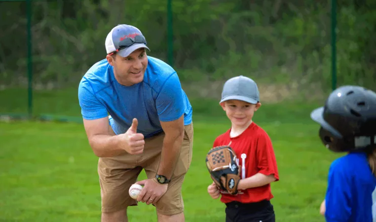 Youth Sports - A volunteer baseball coach gives the thumbs up to his player during a tball game at the YMCA in Chester County.