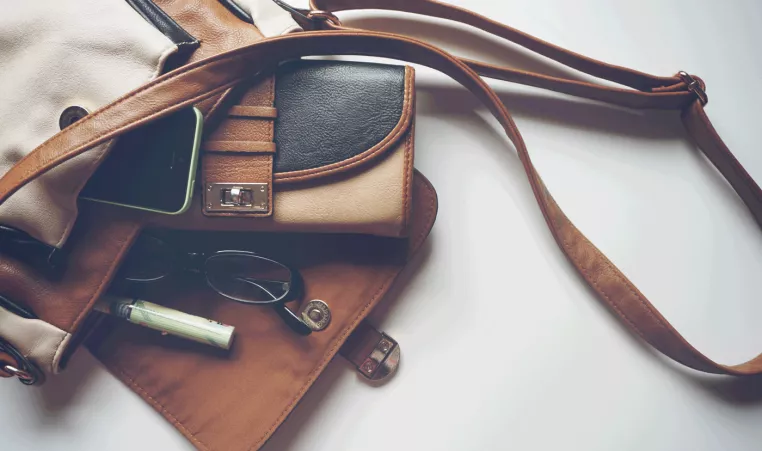A tan purse with wallet, phone and glasses.