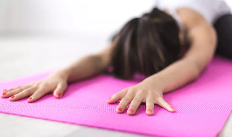 A woman practices Yoga on a pink Yoga mat. 