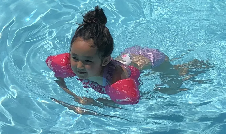 A girls uses a puddle jumper personal flotation device in the outdoor swimming pool