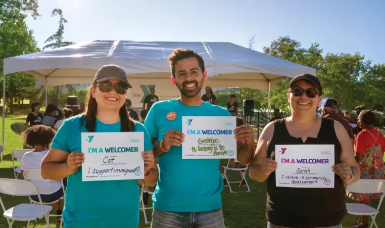 Three YMCA employees standing with signs that read, "I'm A Welcomer." for Welcoming Week