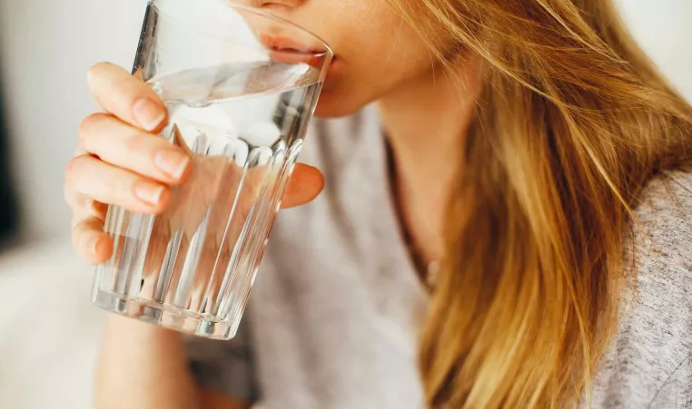 A woman drinks from a clear glass full of water.
