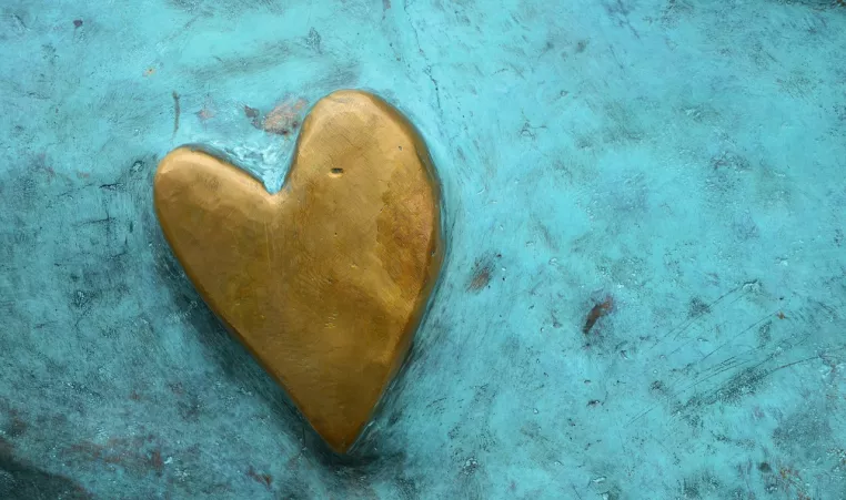 A raised gold shaped heart is shown on a teal background