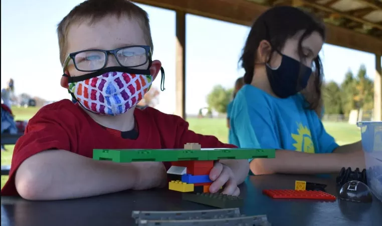 A YMCA summer camp camper wearing a face mask plays with legos during an activity at his camp.