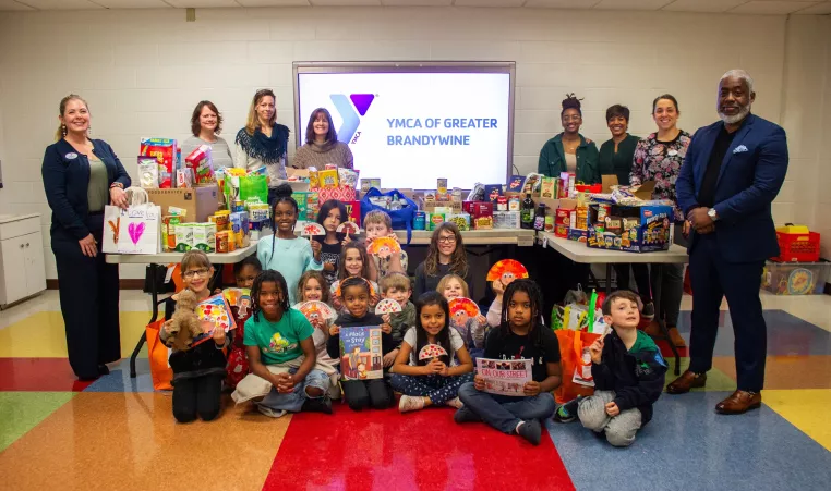 Students from the YMCA's BASE program are pictured with the donations they collected on behalf of local organizations. Pictured with the students (left to right) are Claudia Aust of the YMCA, Ruby Abouraya of Safe Harbor of Chester County, Kecia Crowl of Kennett Area Community Service, Rachel Thomas Steadman of Bridge of Hope, Chaleena Boggs of Safe Harbor of Chester County, Patrice Stilley of Meals on Wheels of Chester County, Laura Mackiewicz of the YMCA and Bertram L. Lawson, II of the YMCA.