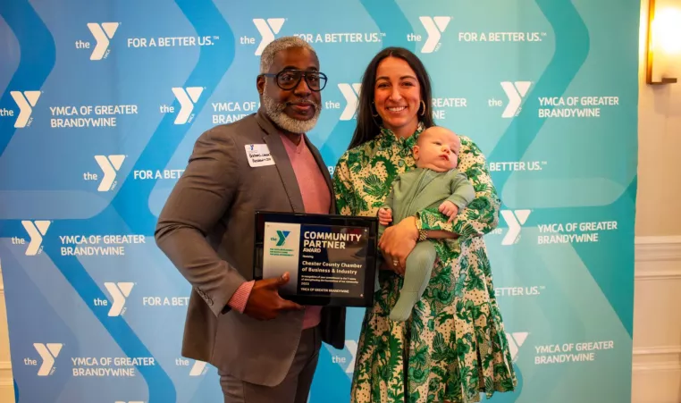 Bertram L. Lawson II, President and CEO of YGBW, presents the YMCA Community Partner Award to Laura Manion, pictured with her newborn son, on behalf of the Chester County Chamber of Business and Industry.