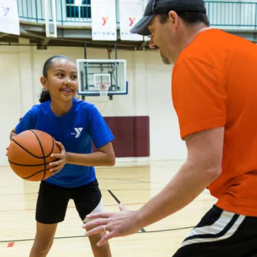A girl practices basketball drills with her basketball coach at the YMCA