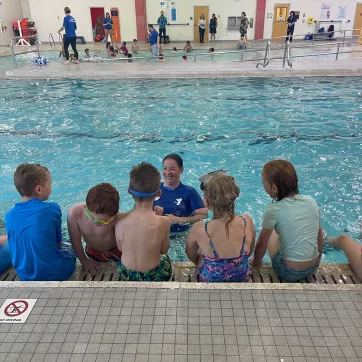 A swim instructor leads children through safety around water programming