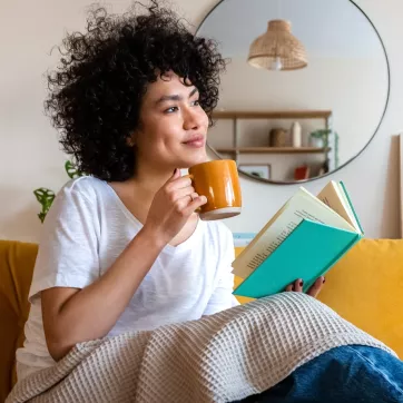 woman sits on couch with a book and cup of tea